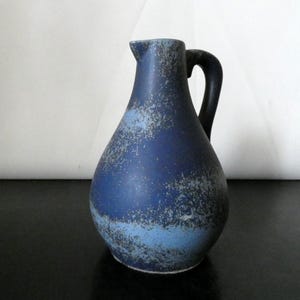 Könnte beinhalten: Eine weiße Keramiktasse mit schwarzem Henkel und dem Text "But First, Coffee" in schwarzer, fetter Schrift. Die Tasse steht auf einer weißen Oberfläche.