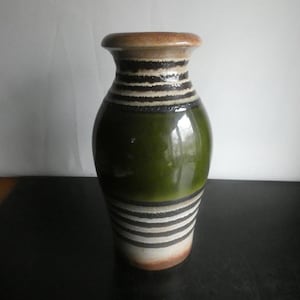 May include: A ceramic vase with a glossy green body and a brown rim. The vase features horizontal black and white striped bands around the neck and base. The vase has a rounded shape and a smooth, reflective surface.