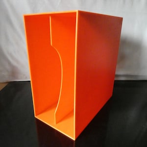 Op de afbeelding: Een feloranje tijdschriftenhouder van kunststof met een rechthoekig frame en een enkele verticale scheidingswand aan de binnenkant. De opening aan de voorzijde heeft een gebogen uitsparing aan de linkerkant voor het opbergen van documenten.