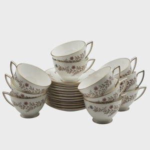 May include: A set of white porcelain teacups and saucers featuring a delicate brown floral vine pattern and gold trim. The collection includes multiple stacked saucers and several teacups arranged around them, each with a curved handle.