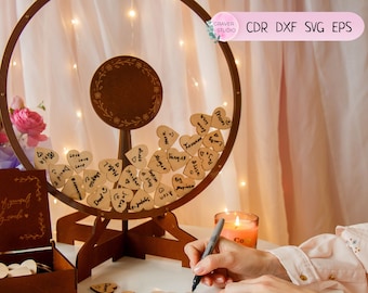 May include: A wooden heart-shaped wish box with a spinning wheel. The wheel is filled with small wooden hearts that guests can write messages on. The box has a sign that reads "Have a piece of yourself in our family code".