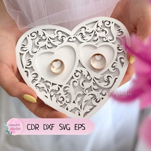 May include: White wooden heart-shaped ring holder with intricate cut-out designs. The holder has two heart-shaped compartments for rings.  CDR DXF SVG EPS