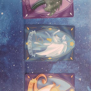 May include: Three fantasy art cards featuring dragons and text. The top card has a green dragon with the text "MOONWATCHER". The middle card has a white dragon with the text "WINTER". The bottom card has a tan dragon with the text "QIBLI".