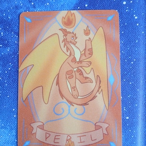 May include: A rectangular card with a cartoon dragon illustration. The dragon is orange and yellow, holding a flame. The word "PERIL" is written on a banner at the bottom. The card has an orange border with blue accents. The background is blue.