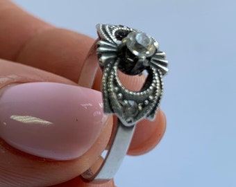 May include: A silver ring with a clear stone set in a decorative filigree design.