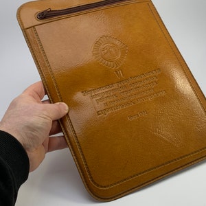 Puede incluir: Una carpeta de cuero marrón con cierre de cremallera y texto en relieve que dice "VI Всесоюзная конференция профсоюзов работников строительства и промышленности строительных материалов Июнь 1931".