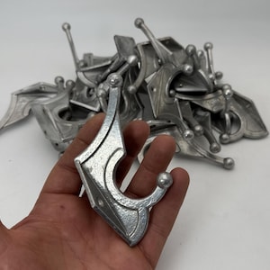 May include: A collection of silver-colored metal coat hooks with an ornate design. The hooks have a decorative, curved shape with a ball at the end of the hook. The hooks are shown on a white background.