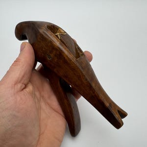 Puede incluir: Una escultura de pájaro de madera tallada a mano con un acabado marrón oscuro. El pájaro está posado con las alas extendidas y la cabeza inclinada hacia un lado.