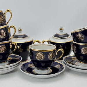 May include: A navy blue tea set with gold detailing. The set includes cups, saucers, and sugar bowls. Each item features a gold floral pattern and gold trim. The handles and rims of the cups and sugar bowls are also gold.