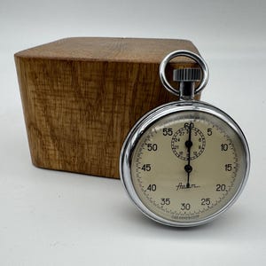 May include: A silver pocket watch with a white face and black markings. The watch has a black hand and a black second hand. The watch face reads "Asam" and "Cazam & Bocek".