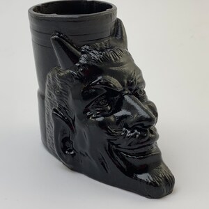 Puede incluir: Taza de cerámica negra con forma de cabeza de diablo con cuernos, barbilla puntiaguda y una sonrisa traviesa.