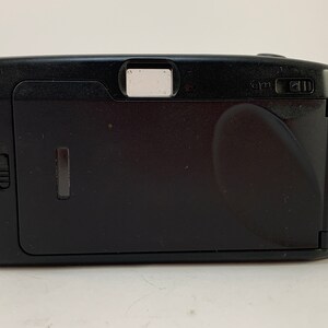 May include: Black compact film camera with a built-in flash. The camera has a small viewfinder on the top and a lens cover on the front.