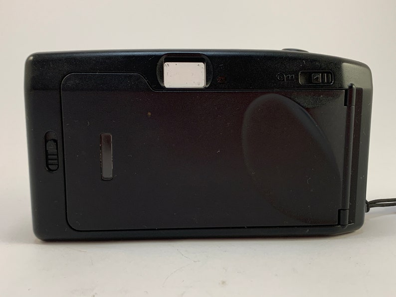 May include: Black compact film camera with a built-in flash. The camera has a small viewfinder on the top and a lens cover on the front.