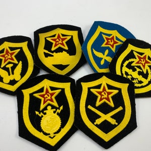 May include: Six embroidered patches with a shield shape and a red star with a hammer and sickle. Each patch has a different symbol in the center, including a tank, a plane, a cannon, and a ship.