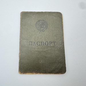 May include: An olive green passport with the Cyrillic word "ПАСПОРТ" printed in black. The passport has a faded emblem at the top and a worn, textured appearance. The edges are a faded yellow.