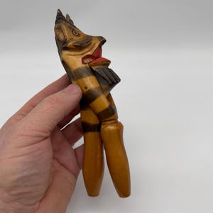 以下が含まれることがあります： 縞模様の体と彫刻された顔を持つ木製のナッツクラッカー。ナッツクラッカーは茶色、黒、赤の色合いで塗られています。