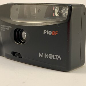 May include: A black Minolta F10BF point and shoot camera with a built-in flash. The camera has a red eye reduction feature and a viewfinder.