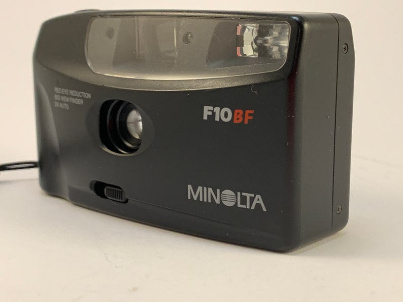 May include: A black Minolta F10BF point and shoot camera with a built-in flash. The camera has a red eye reduction feature and a viewfinder.