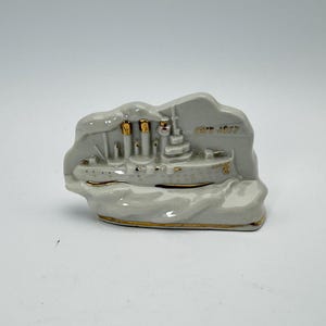 May include: A ceramic figurine of a ship, likely a cruise liner, emerging from a stylized iceberg. The ship is white with gold accents, including the smokestacks. The figurine has the text "1912-1912" in gold.