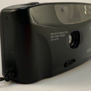 May include: A black Minolta F10X point-and-shoot camera with a red eye reduction feature, a big view finder, and DX auto. The camera has a black strap attached.