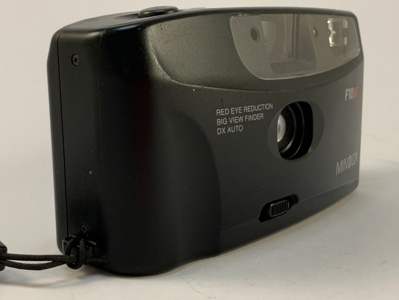 May include: A black Minolta F10X point-and-shoot camera with a red eye reduction feature, a big view finder, and DX auto. The camera has a black strap attached.