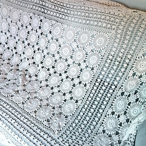May include: A white crochet blanket featuring a repeating circular floral motif pattern. The textile is constructed with intricate openwork stitching, creating a delicate lace-like texture throughout the entire surface of the rectangular fabric piece.