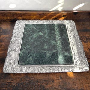 May include: A square serving tray featuring a dark green marble center inlay surrounded by a metallic silver-toned border. The border is embossed with detailed relief figures of various animals including lions, rabbits, and turtles.