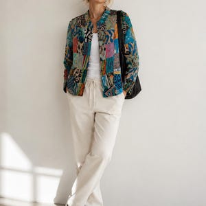 Puede incluir: Una chaqueta de manga larga con un vibrante estampado de patchwork en tonos azules, verde azulado, naranja y rosa. La chaqueta se lleva sobre una camiseta de tirantes blanca lisa y se combina con pantalones de color crema con cord&oacute;n y zapatillas blancas.