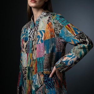May include: A long-sleeve quilted jacket featuring a vibrant patchwork design with various multicoloured patterns, including blue, yellow, orange, and black. The jacket has a mandarin collar, a front button closure, and two lower front pockets.