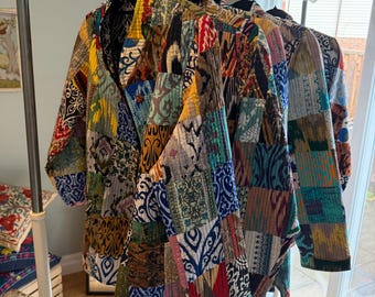Puede incluir: Una colección de tres chaquetas acolchadas colgadas en un perchero de metal. Cada chaqueta presenta un diseño de patchwork compuesto por varios cuadrados de tela en colores vibrantes como amarillo, azul, rojo y verde, con patrones y costuras intrincadas.