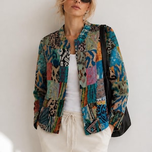 Puede incluir: Una chaqueta acolchada con un dise&ntilde;o de patchwork vibrante que presenta varios patrones abstractos en tonos azul, verde azulado, naranja y negro. La chaqueta tiene un cuello redondo, mangas largas y un dobladillo recto, sobre una camiseta blanca.