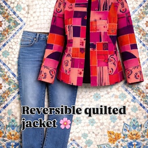 Op de afbeelding: Een omkeerbaar gewatteerd jack in roze, oranje en paarse tinten, gecombineerd met een blauwe jeans en een zwarte zonnebril. De jas heeft een patchwork-ontwerp. De tekst "Reversible quilted jacket" wordt weergegeven.