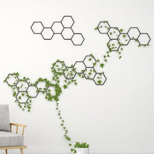 May include: A white room with a gray armchair, a gold floor lamp, and a wall with a black geometric design covered in green vines.