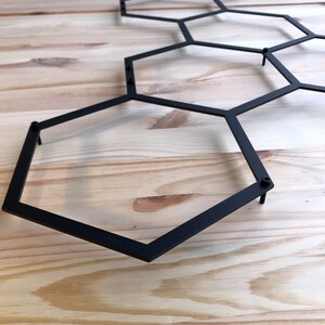 May include: Black metal hexagonal wall decor with a geometric design. The decor is made of thin metal rods that are connected to form a honeycomb pattern.