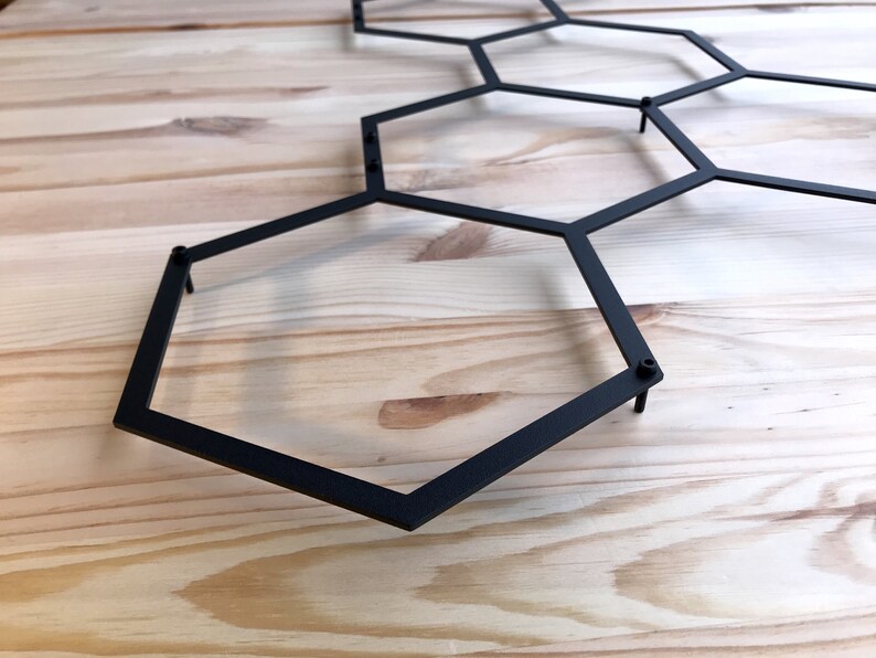 May include: Black metal hexagonal wall decor with a geometric design. The decor is made of thin metal rods that are connected to form a honeycomb pattern.
