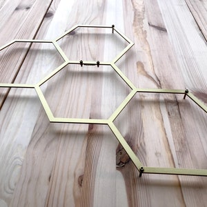 May include: A gold metal honeycomb-shaped wall decor with six hexagonal sections. The decor is mounted on a light wood surface.