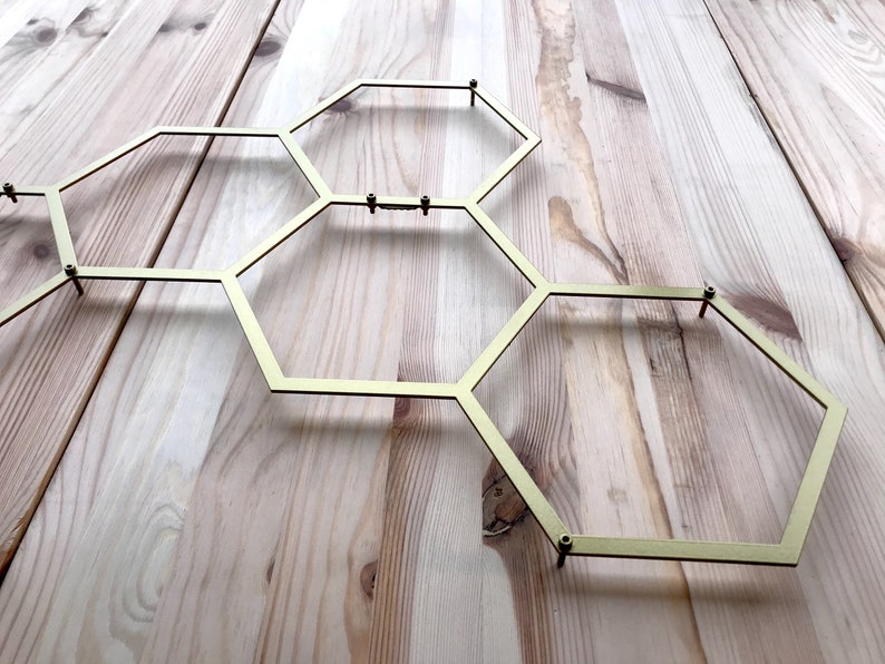 May include: A gold metal honeycomb-shaped wall decor with six hexagonal sections. The decor is mounted on a light wood surface.