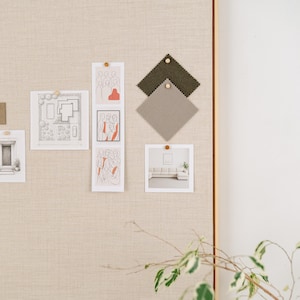 May include: A neutral-toned mood board with architectural sketches, fabric swatches, and art prints. The board is pinned with wooden push pins. A sprig of greenery is in the foreground.