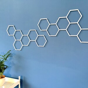 May include: White honeycomb-shaped wall decor made of metal. The decor is arranged in a staggered pattern on a light blue wall.