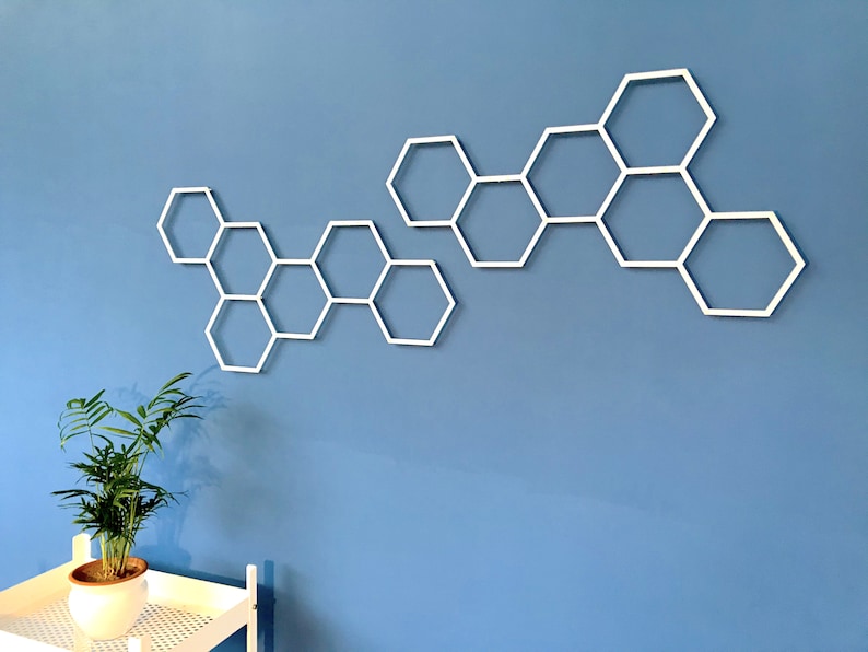 May include: White honeycomb-shaped wall decor made of metal. The decor is arranged in a staggered pattern on a light blue wall.