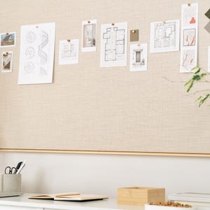 May include: A neutral-toned bulletin board with various architectural sketches and design samples pinned to it. A wooden artist's mannequin, a laptop, and stationery are on the desk below. The overall theme is interior design and planning.