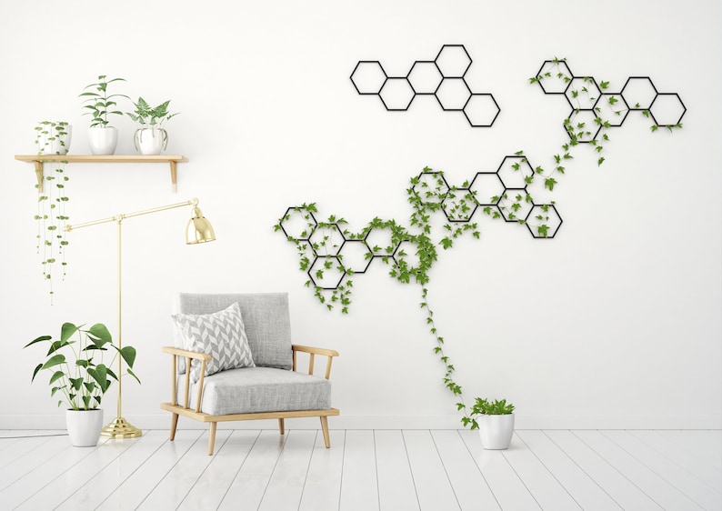 May include: A white room with a gray armchair, a gold floor lamp, and a wall with a black geometric design covered in green vines.
