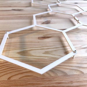 May include: White metal hexagonal geometric wall decor with a modern design. The decor is made of thin metal and has a simple, minimalist style.