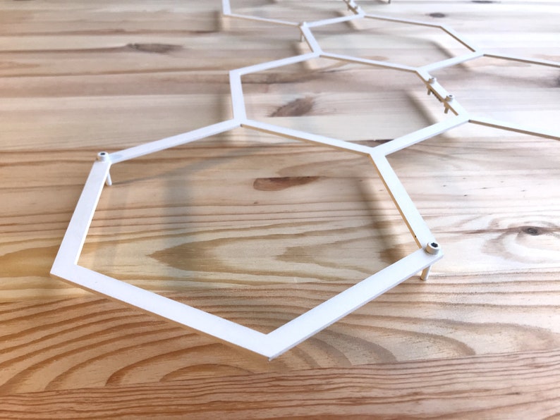 May include: White metal hexagonal geometric wall decor with a modern design. The decor is made of thin metal and has a simple, minimalist style.