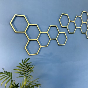 May include: Gold honeycomb wall decor with a geometric design. The honeycomb is made of metal and is attached to a blue wall.