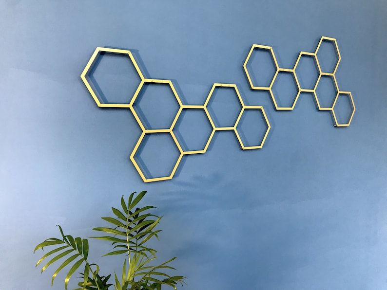 May include: Gold honeycomb wall decor with a geometric design. The honeycomb is made of metal and is attached to a blue wall.
