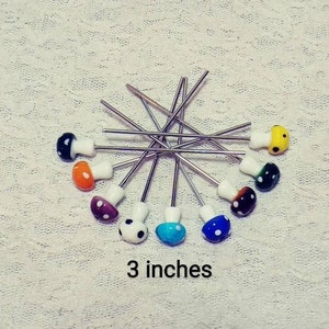 May include: A set of 12 colorful mushroom-shaped glass beads on silver wire stems. The beads are 3 inches long and feature various colors, including yellow, orange, brown, blue, and black.