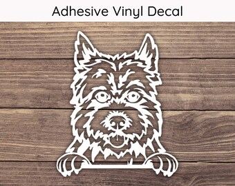 May include: White adhesive vinyl decal of a dog's face with the text "Adhesive Vinyl Decal" at the top. The dog's face is detailed with eyes, nose, and paws. The decal is on a wooden background.