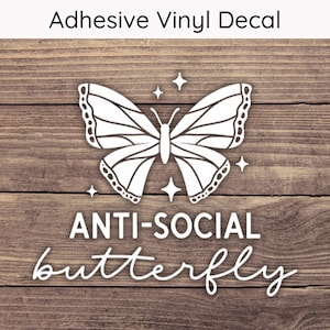 May include: White adhesive vinyl decal featuring a butterfly design with the words "ANTI-SOCIAL butterfly". The decal includes four star accents and the text "Adhesive Vinyl Decal" at the top. The background is a wood grain pattern.