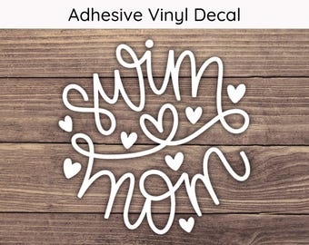 May include: White adhesive vinyl decal with the words "Swim Mom" in a cursive font, surrounded by small heart shapes. The decal is set against a wooden background, with the text "Adhesive Vinyl Decal" at the top.